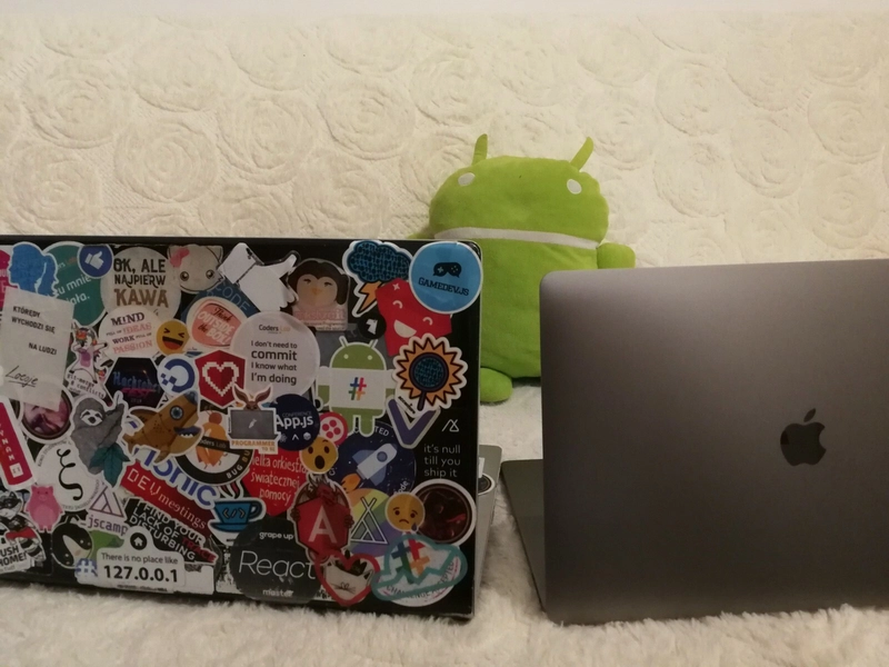 毛绒玩具 Android 坐在两台电脑前 - 其中一台完全贴满贴纸，另一台上没有贴纸。