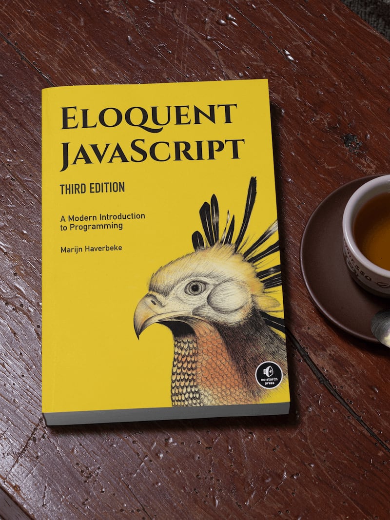 乡村风格的桌子上放着一本厚厚的平装版《Eloquent Javascript》，旁边是一杯咖啡。