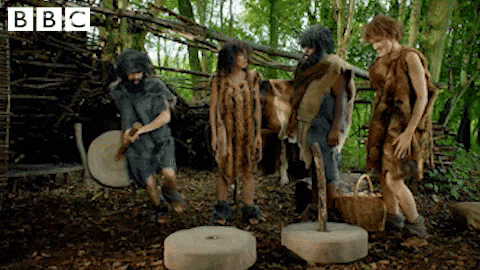 两个穴居人惊奇地看着另一个穴居人建造轮子和轴的 GIF
