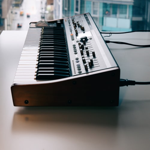 这张 Midi 键盘的照片是从侧面拍摄的，它放在窗边的桌子上。背景是一条空荡荡的街道。